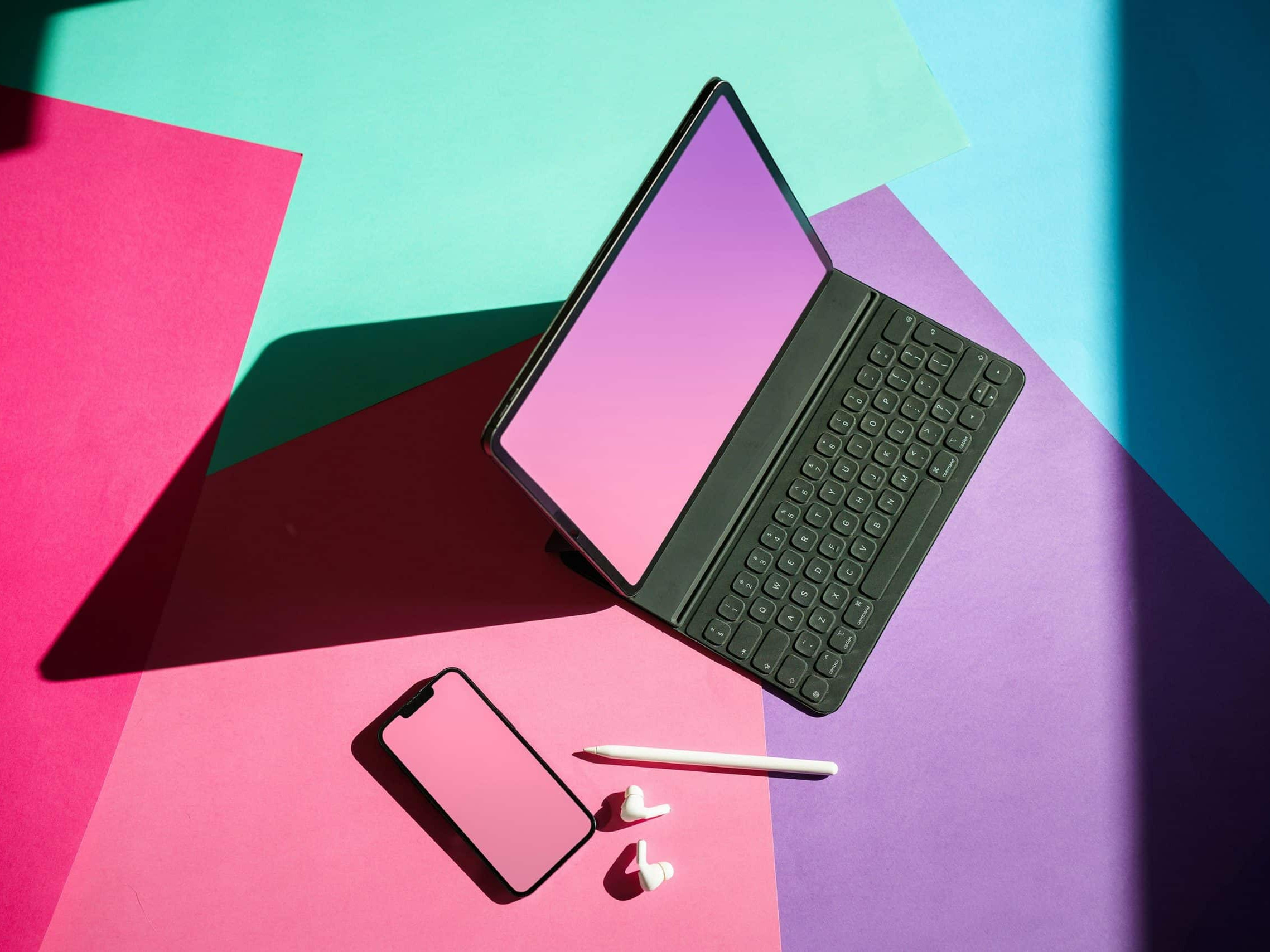 Ein heller und farbenfroher Hintergrund aus Blau, Türkis, Rosa und Lila. Oben auf den Farben sitzen ein Laptop, einige weiße Ohrstöpsel, ein Telefon und ein intelligenter Bleistift. Verwendet zur Illustration eines Abschnitts über Mulimedia als Teil unseres Artikels über SEO-freundlichen Webaufbau.